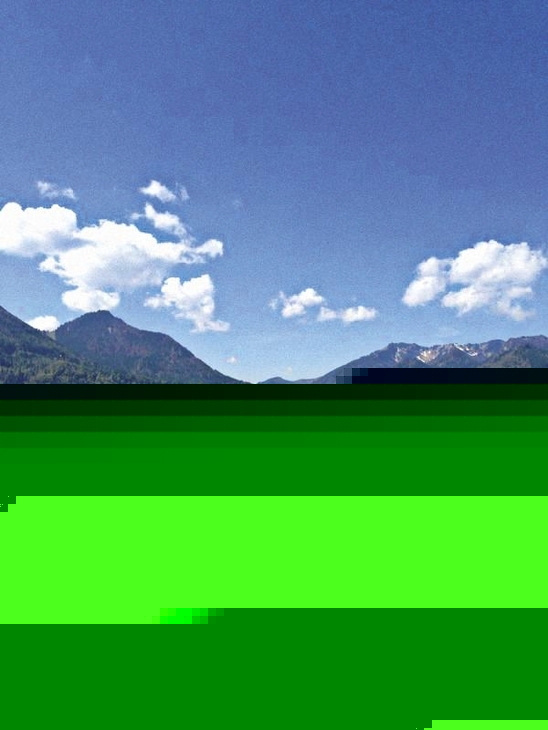 Landschaft bei Inzell mit Bergen und Wiesen unter blauem Himmel.