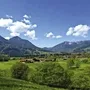 Landschaft bei Inzell mit Bergen und Wiesen unter blauem Himmel.