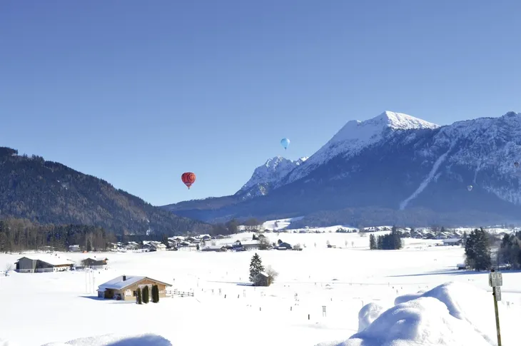 Winterliche Alpenlandschaft mit Heißluftballons am Himmel.