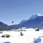 Winterliche Alpenlandschaft mit Heißluftballons am Himmel.