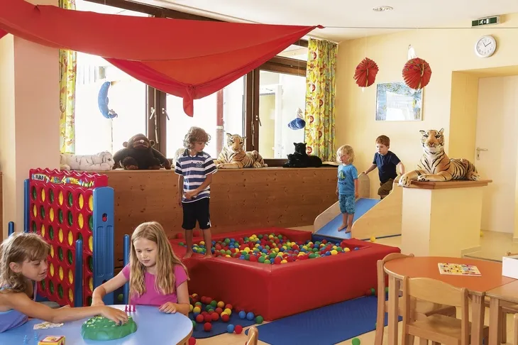 Kinder spielen in einem bunten Spielzimmer mit Bällebad und Plüschtigern.