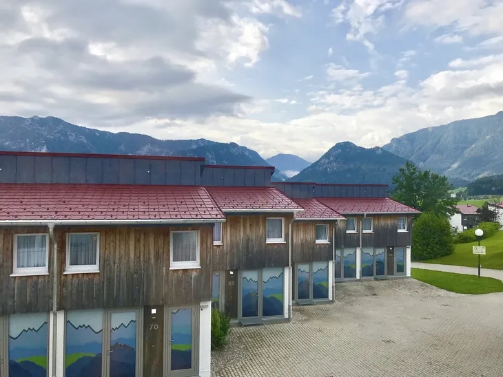 Mehrere Holzgebäude mit Bergen im Hintergrund unter bewölktem Himmel.