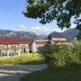 Gebäude vor Berglandschaft mit klarem Himmel und Bäumen im Vordergrund.