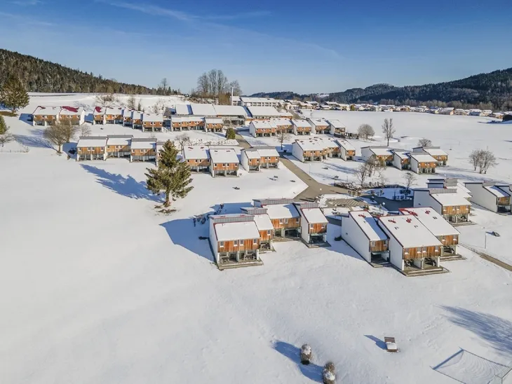 Verschneite Häuser in Inzell, umgeben von winterlicher Landschaft und blauem Himmel.