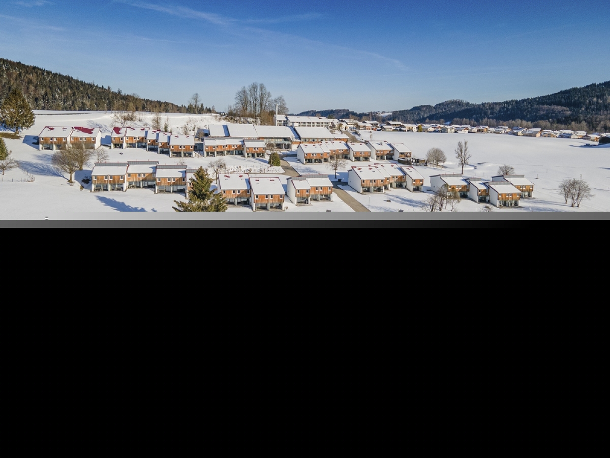 Verschneite Häuser in Inzell, umgeben von winterlicher Landschaft und blauem Himmel.