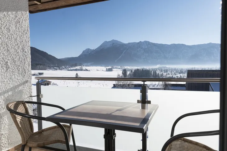 Balkon mit Tisch und Stühlen, Blick auf verschneite Berglandschaft bei klarem Himmel.