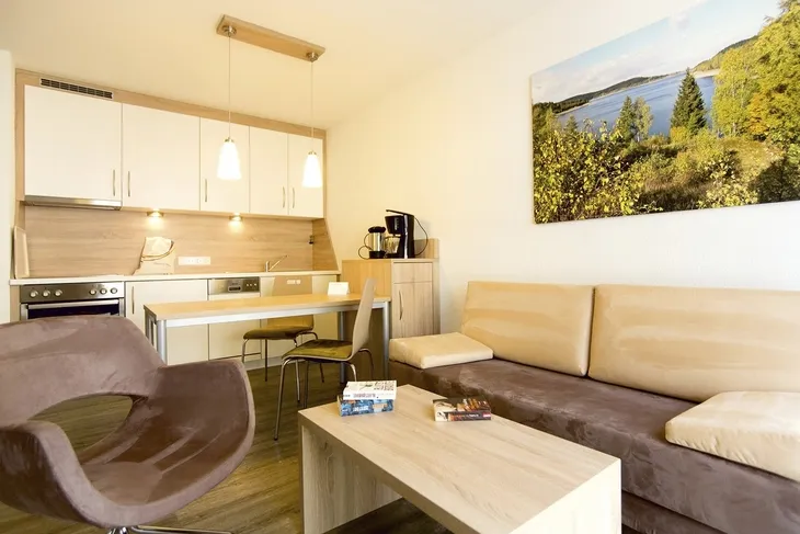 Wohnbereich mit Küche, Esstisch, Stühlen, Sofa, Sessel, Tisch und Wandbild in Ferienanlage Braunlage.