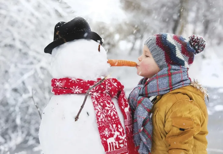 Kind küsst Schneemann auf Karottennase im Winter.