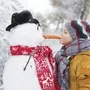 Kind küsst Schneemann auf Karottennase im Winter.