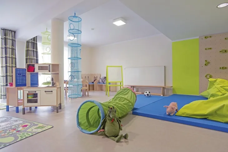 Helles Spielzimmer mit Spielzeug, Tunnel, blauer Turnmatte und Kinderküche in der Ferienanlage Braunlage.