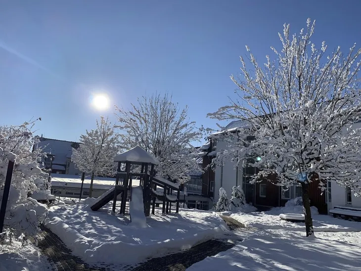 Verschneiter Spielplatz mit strahlender Sonne, blauem Himmel und schneebedeckten Bäumen in der Ferienanlage Braunlage .