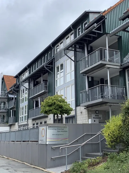 Eingangsbereich mit Treppe zu einem mehrstöckigen, modernen Gebäude der Ferienanlage Braunlage mit Balkonen.