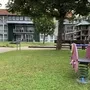 Spielplatz mit Wipptier und Spielturm auf einer Wiese vor einem Gebäude der Ferienanlage Braunlage.