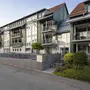 Mehrstöckiges Gebäude mit Balkonen und grünem Anstrich, umgeben von Pflanzen.
