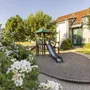 Spielplatz mit Rutsche in einer Gartenanlage vor einem Gebäude am sonnigen Tag.
