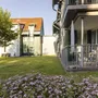Garten mit Blumenteppich vor einem Gebäude mit Balkon bei sonnigem Wetter.
