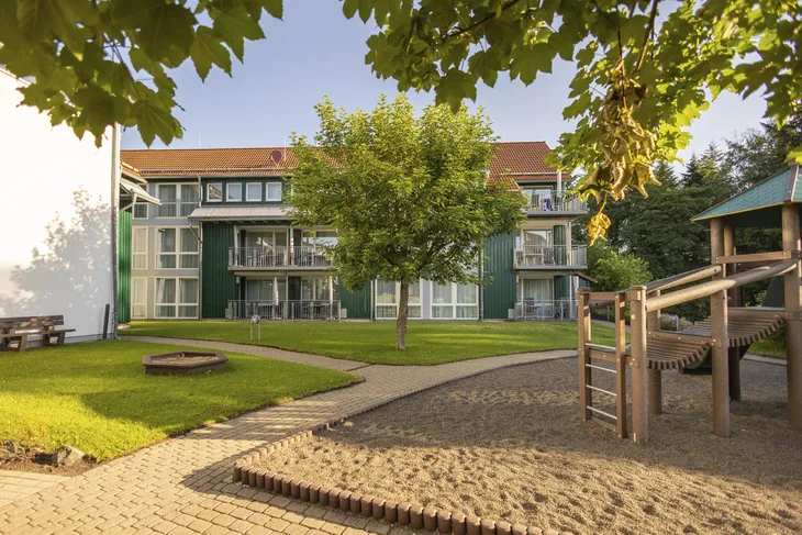 Gebäude mit Rasenfläche, Baum und Spielplatz im Vordergrund.