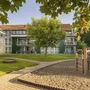 Gebäude mit Rasenfläche, Baum und Spielplatz im Vordergrund.