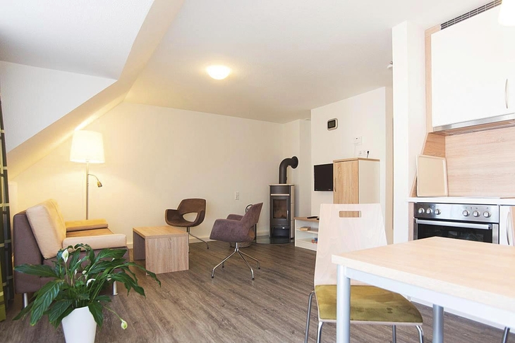 Wohnzimmer mit Kamin, Stühlen, Tisch und Küche in Braunlage.