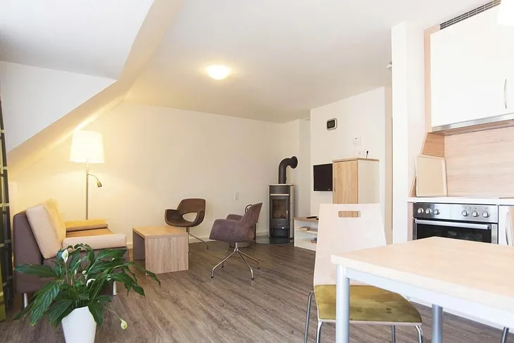 Wohnzimmer mit Kamin, Stühlen, Tisch und Küche in Braunlage.