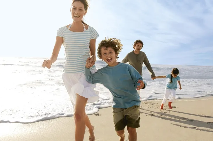 Eine lachende Familie, mit zwei Kindern, läuft am Strand entlang.