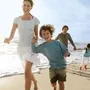 Eine lachende Familie, mit zwei Kindern, läuft am Strand entlang.
