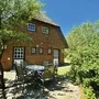 Reedgedecktes Backsteinhaus mit Tisch und Stühlen davor, bei blauem Himmel umgeben von Bäumen, in der Ferienanlage List auf Sylt.