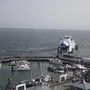 Hafenansicht mit mehreren Booten und einer Fähre im Hintergrund.
