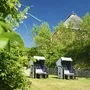 Zwei Strandkörbe auf einer grünen Wiese, von Bäumen umgeben und blauem Himmel, vor einem Backsteinhaus mit Reetdach.