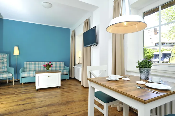Wohnzimmer mit Holztisch, blauem Sofa, TV, und Stehlampe in Ferienwohnung.