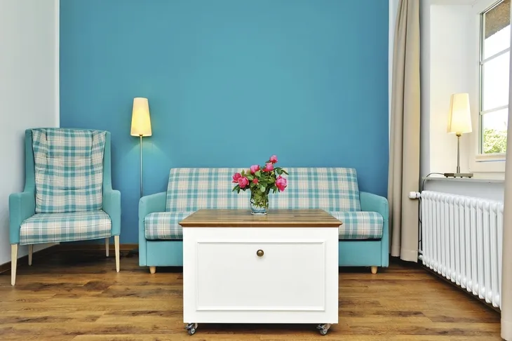 Wohnzimmer mit blauer Wand, kariertem Sofa, Sessel, Tisch und Blumenstrauß.