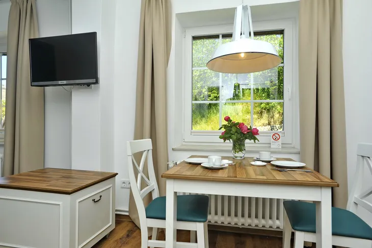 Essbereich mit Holztisch, zwei Stühlen, Lampe, Fenster und TV an der Wand.