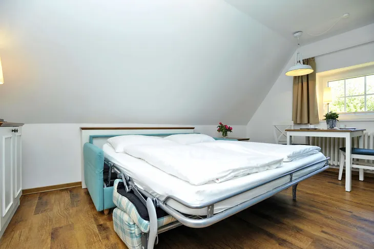 Zimmer mit ausgezogenem Schlafsofa, Esstisch und Fenster.