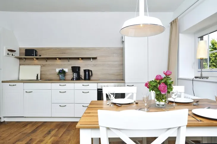 Helle Küche mit Esstisch, weißen Möbeln und einem Blumenstrauß.