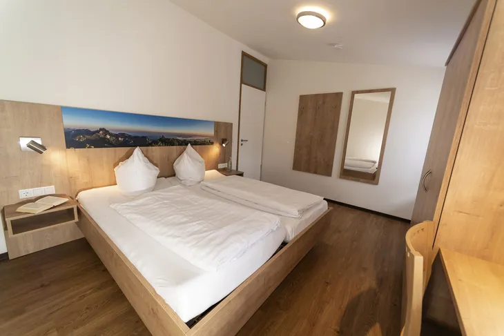 Doppelbettzimmer mit Holzmöbeln und Bergpanoramabild an der Wand.