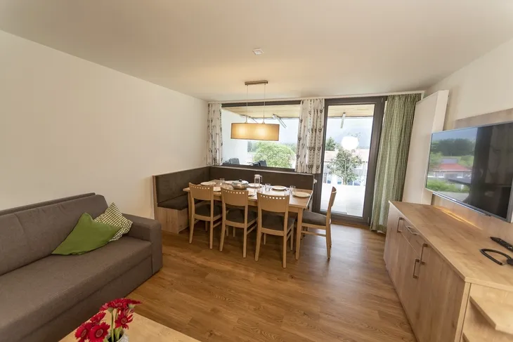 Wohnbereich mit Tisch, Stühlen, Sofa, TV im Ferienhaus, Fenster mit Vorhängen.