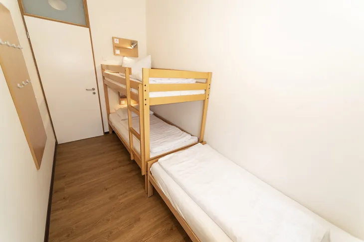 Schlafzimmer mit Etagenbett und Einzelbett in hellem Raum.