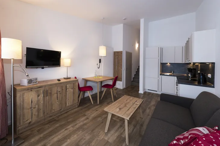 Wohnbereich mit Holzmöbeln, Sofa, Tisch, Stühle und Küchenzeile.