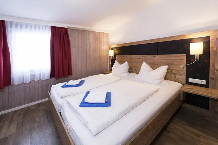 Schlafzimmer mit Doppelbett, Holzverkleidung und roten Vorhängen.