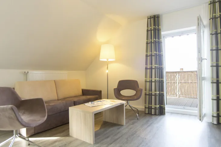 Helles Wohnzimmer mit Sofa, Sesseln, Stehlampe und Zugang zum Balkon.