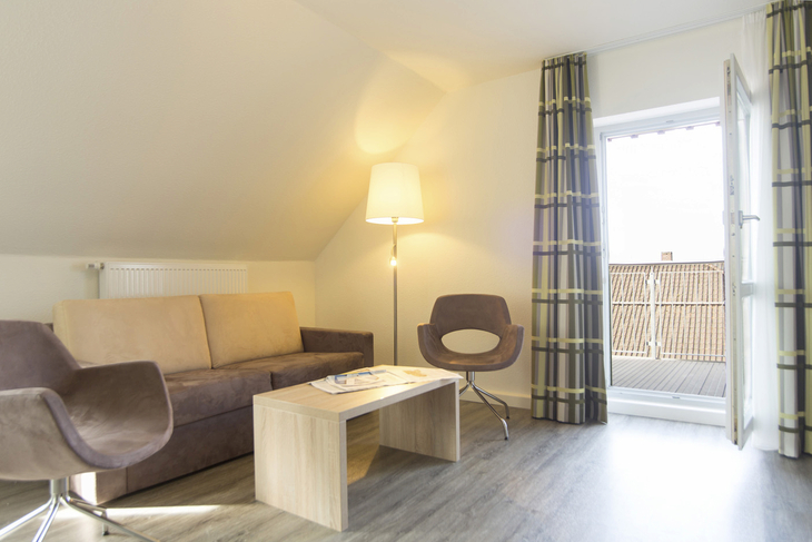 Helles Wohnzimmer mit Sofa, Sesseln, Stehlampe und Zugang zum Balkon.