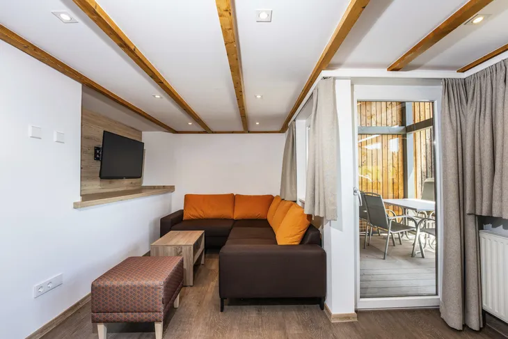 Wohnzimmer mit Ecksofa, Fernseher und Zugang zur Terrasse