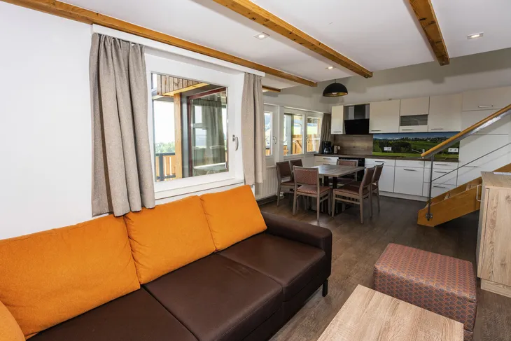 Wohnbereich mit Sofa, Tisch, Küche und Treppe in modernem Design.