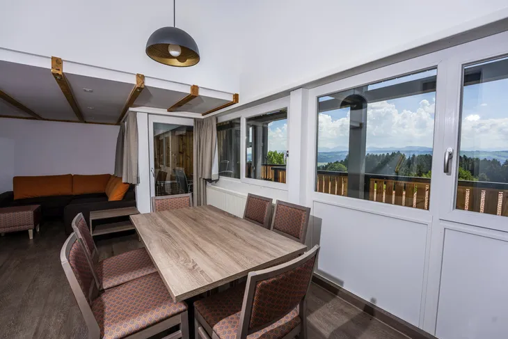 Esszimmer mit großem Tisch, Stühlen und Panoramafenstern mit Bergblick.