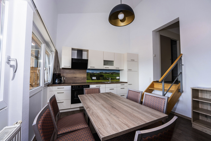 Moderne Küche mit Esstisch, Stühlen und Treppe in einem hellen Raum.