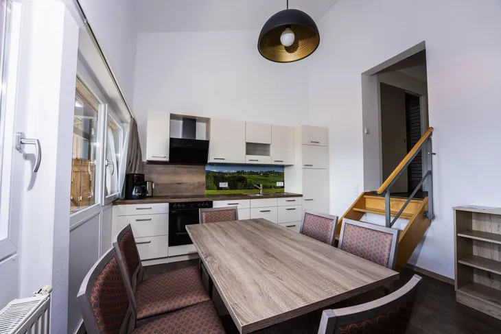 Moderne Küche mit Esstisch, Stühlen und Treppe in einem hellen Raum.