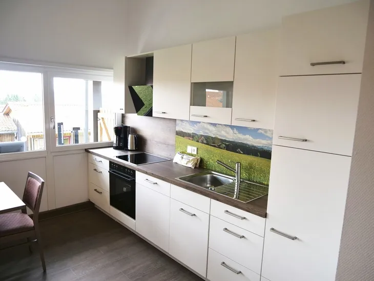Moderne Küche mit weißen Schränken, eingebautem Herd und Landschaftsfoto als Rückwand.