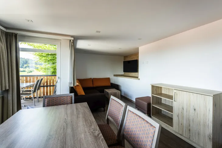 Wohnzimmer mit Esstisch, Stühlen, Sofa und Balkon im Hintergrund.