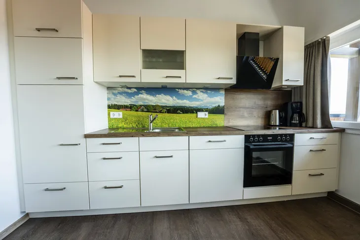Moderne Einbauküche mit hellen Fronten und Landschaftsbild an der Rückwand.