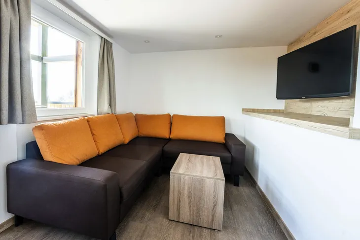 Ecksofa mit orangefarbenen Kissen in einem modernen Wohnzimmer mit Fernseher an der Wand.